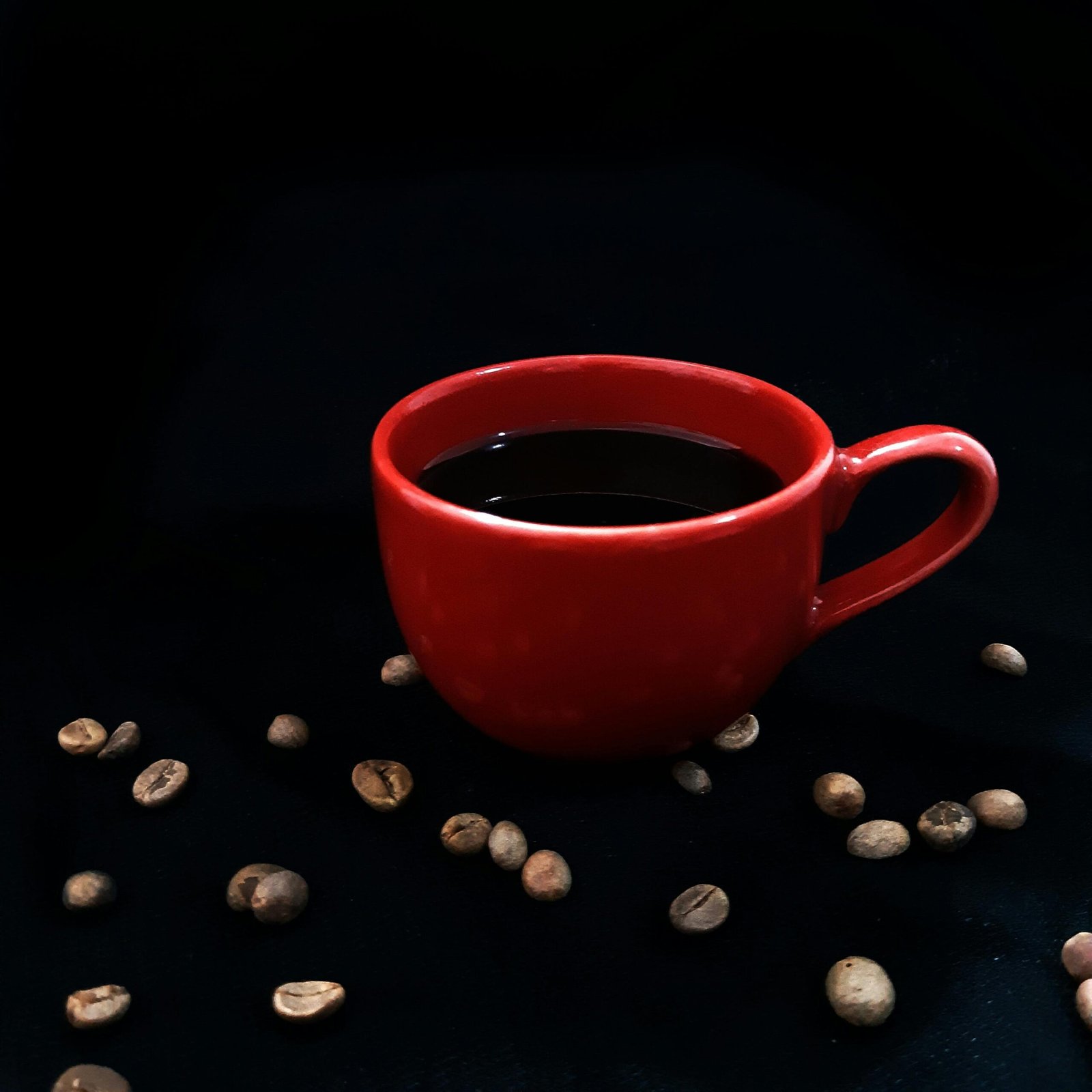 A vibrant red cup filled with black coffee, surrounded by coffee beans on a dark background.