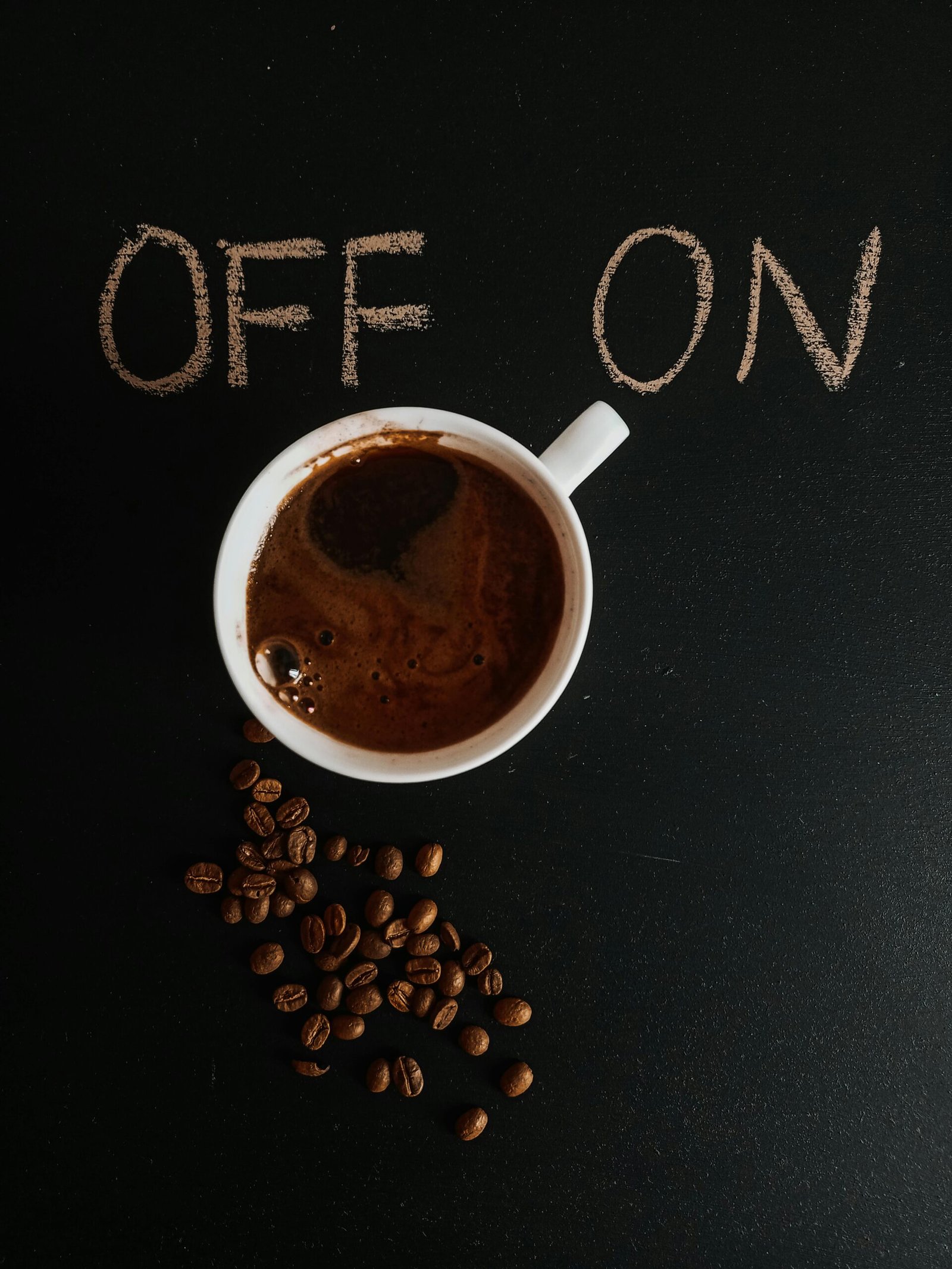 A cup of coffee surrounded by beans and chalk writings 'OFF' and 'ON', symbolizing a caffeine boost.