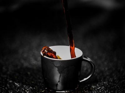 Close-up of steaming dark coffee being poured into a black cup on a dark textured surface. Rich aroma.